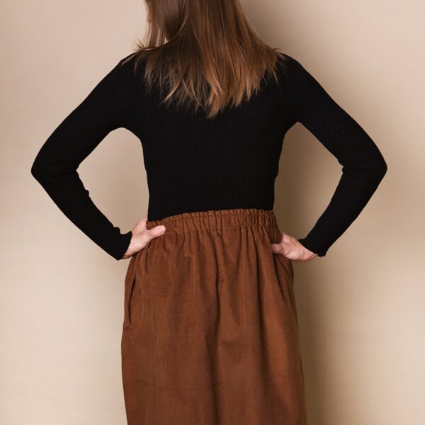Dziewczyna stoi tyłem i ma na sobie sztruksową spódnicę w naturalnym brązowym kolorze dla kobiet.